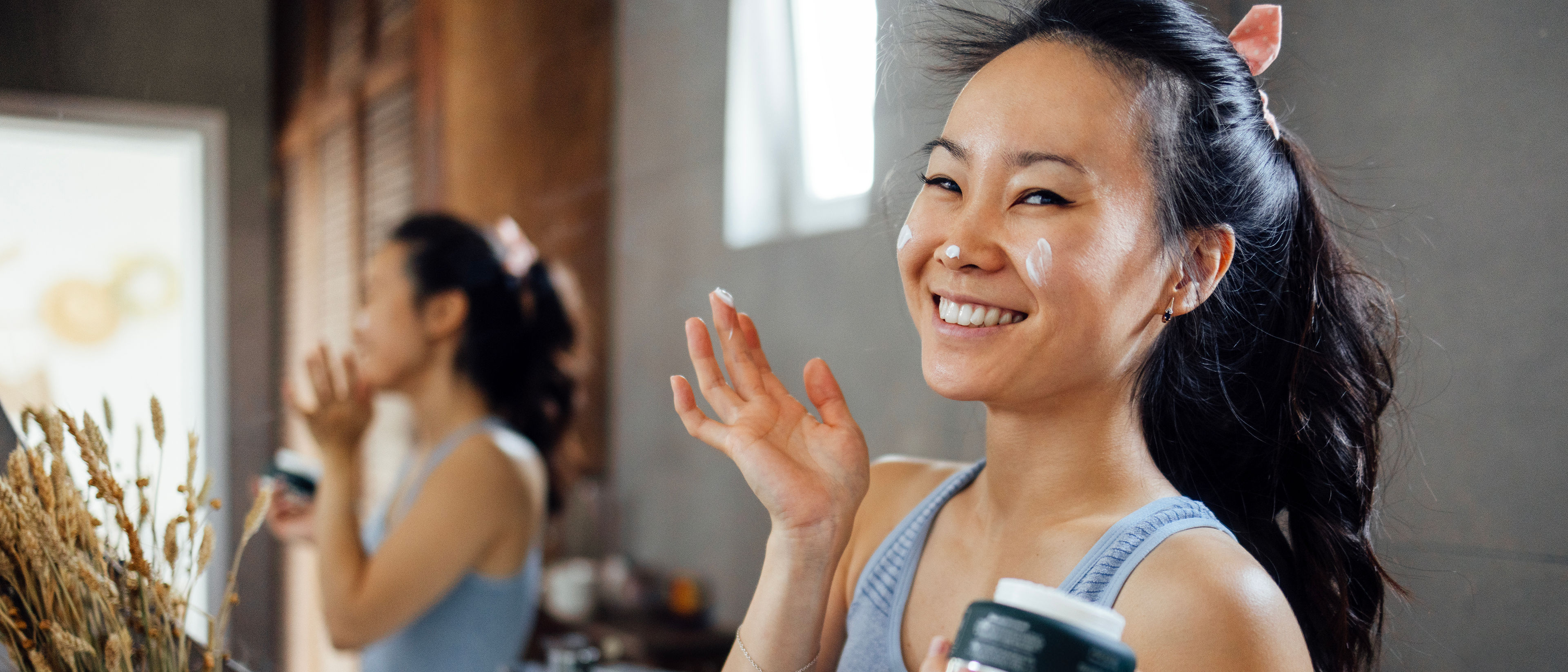 Smiling asian young woman applies moisturizing cream.